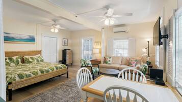 A well-lit room with a bed, a dining table, chairs, a sofa, and a ceiling fan.