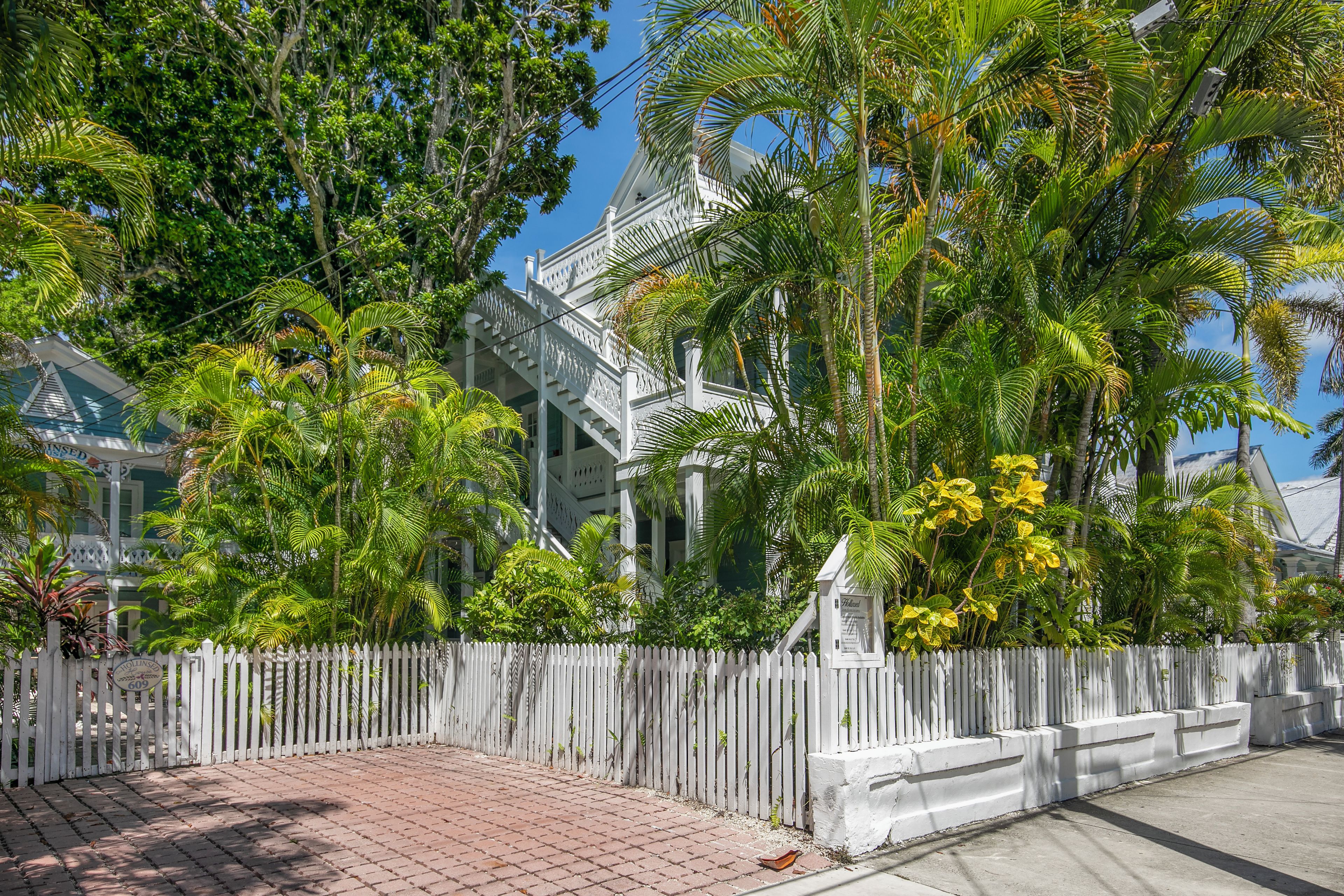 A white building with a traditional architectural style, surrounded by lush greenery and a white picket fence.
