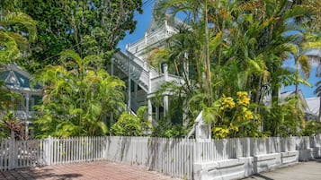 A white building with a traditional architectural style, surrounded by lush greenery and a white picket fence.
