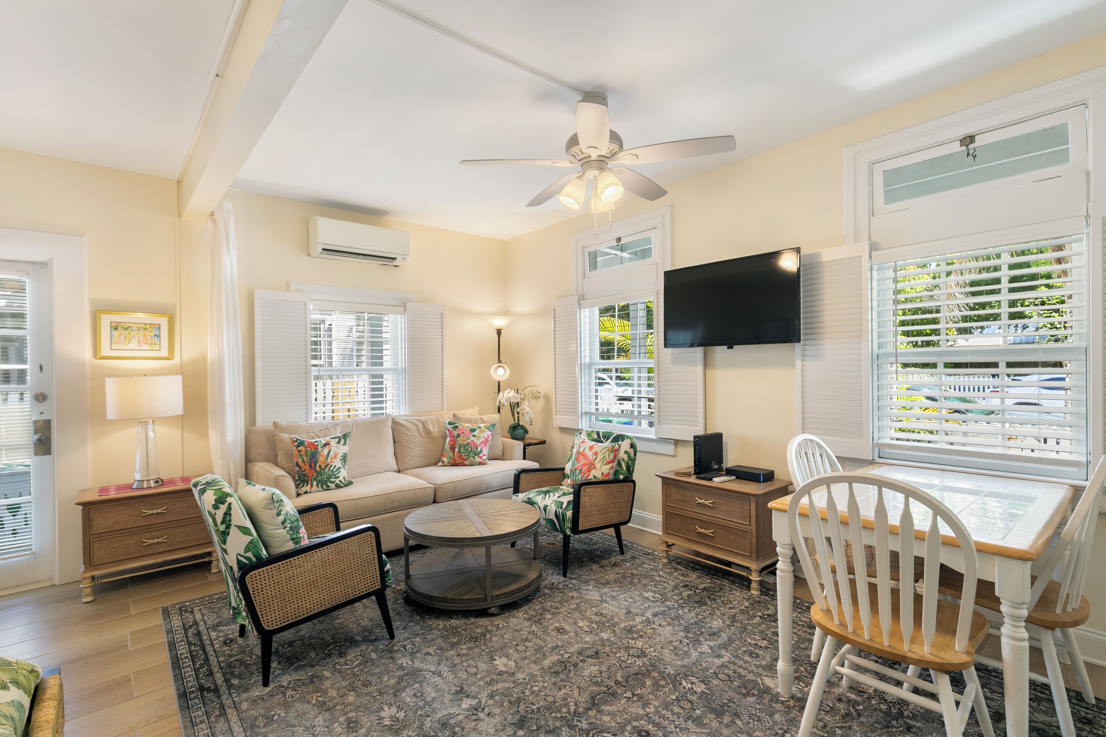 A living room with a sofa, two chairs, a coffee table, a TV, and a ceiling fan.
