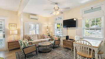 A living room with a sofa, two chairs, a coffee table, a TV, and a ceiling fan.