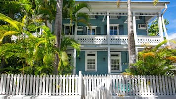 A two-story building with a white picket fence in front, surrounded by lush greenery.