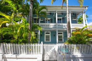 A two-story building with a white picket fence in front, surrounded by lush greenery. - Hollinsed House Studio - Great Location!! (Key West)
