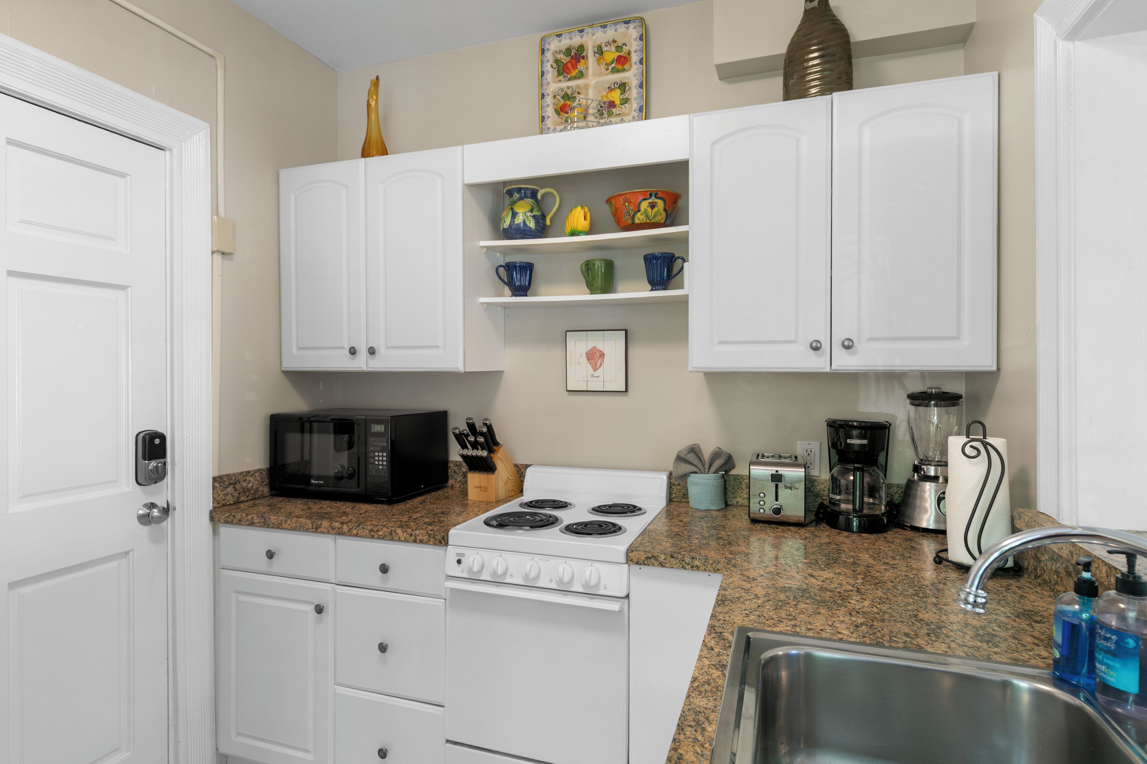 A kitchen with white cabinets, a stove, a microwave, a toaster, and a sink.