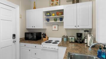 A kitchen with white cabinets, a stove, a microwave, a toaster, and a sink.