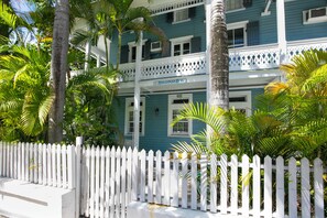 A two-story building with a white picket fence, palm trees, and a sign that reads 'Hollinsed House.' - Hollinsed House Studio - Great Location!! (Key West)