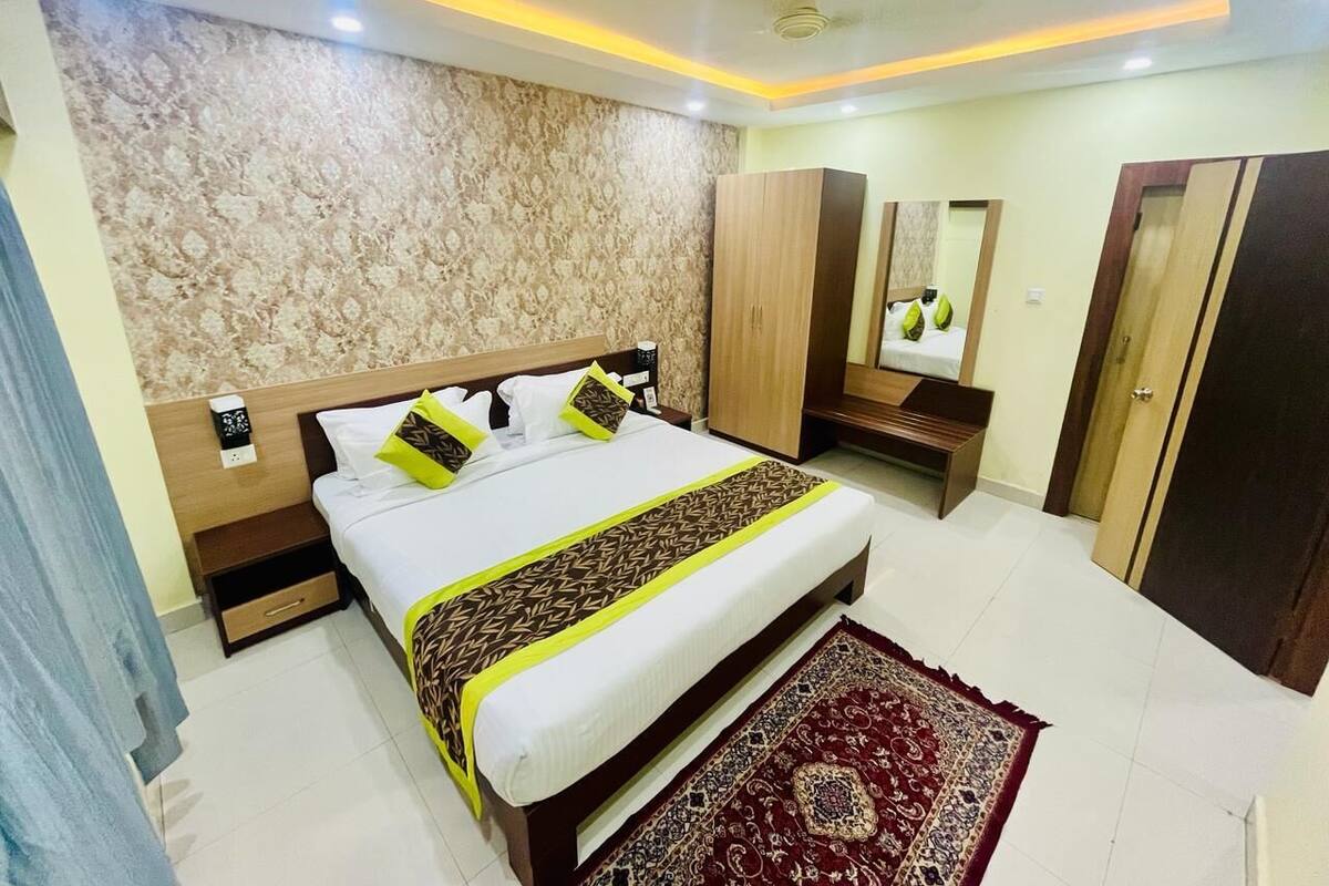 A hotel room with a large bed, a wooden wardrobe, a nightstand, and a mirror.
