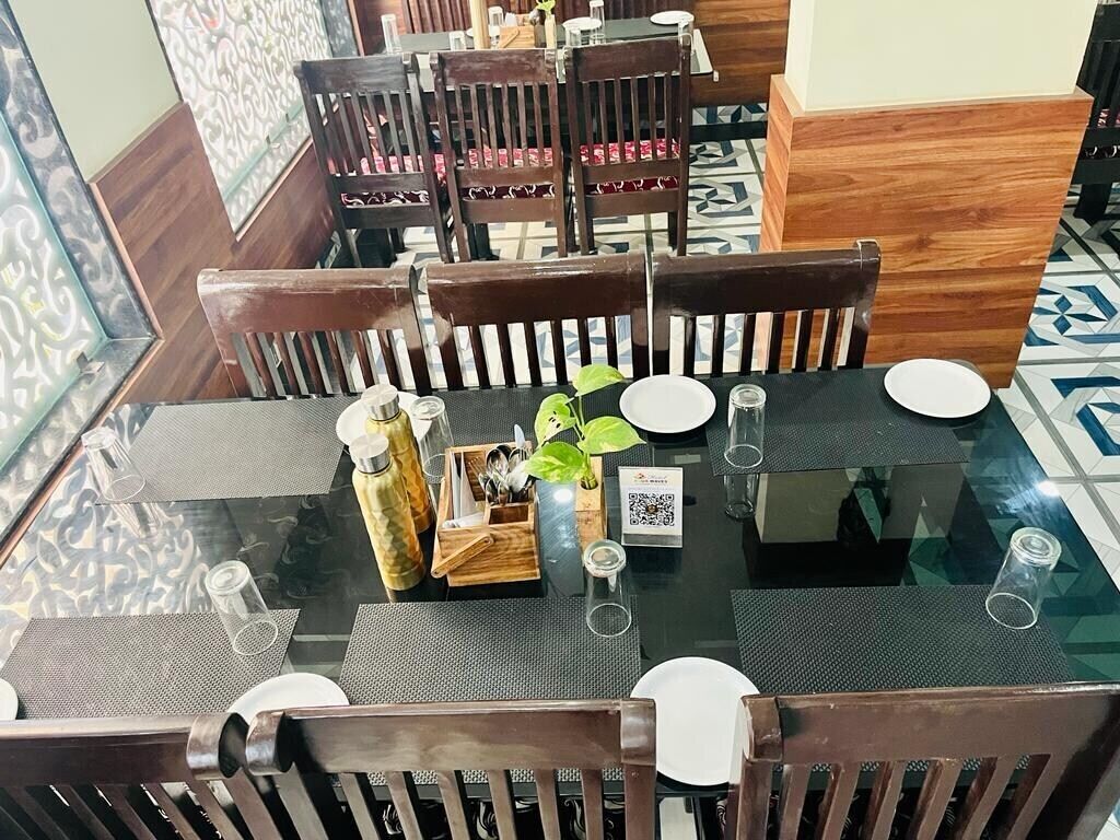 A dining area with a glass table, wooden chairs, and a QR code on the placemat.
