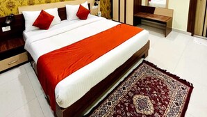 A hotel room with a large bed, a wooden wardrobe, a bedside table, a mirror, and a patterned rug. - Hotel Four Waves (Puri)