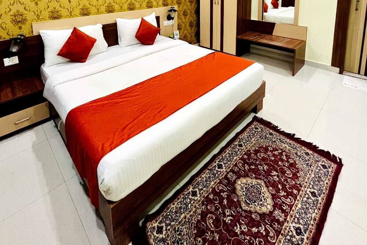 A hotel room with a large bed, a wooden wardrobe, a bedside table, a mirror, and a patterned rug.