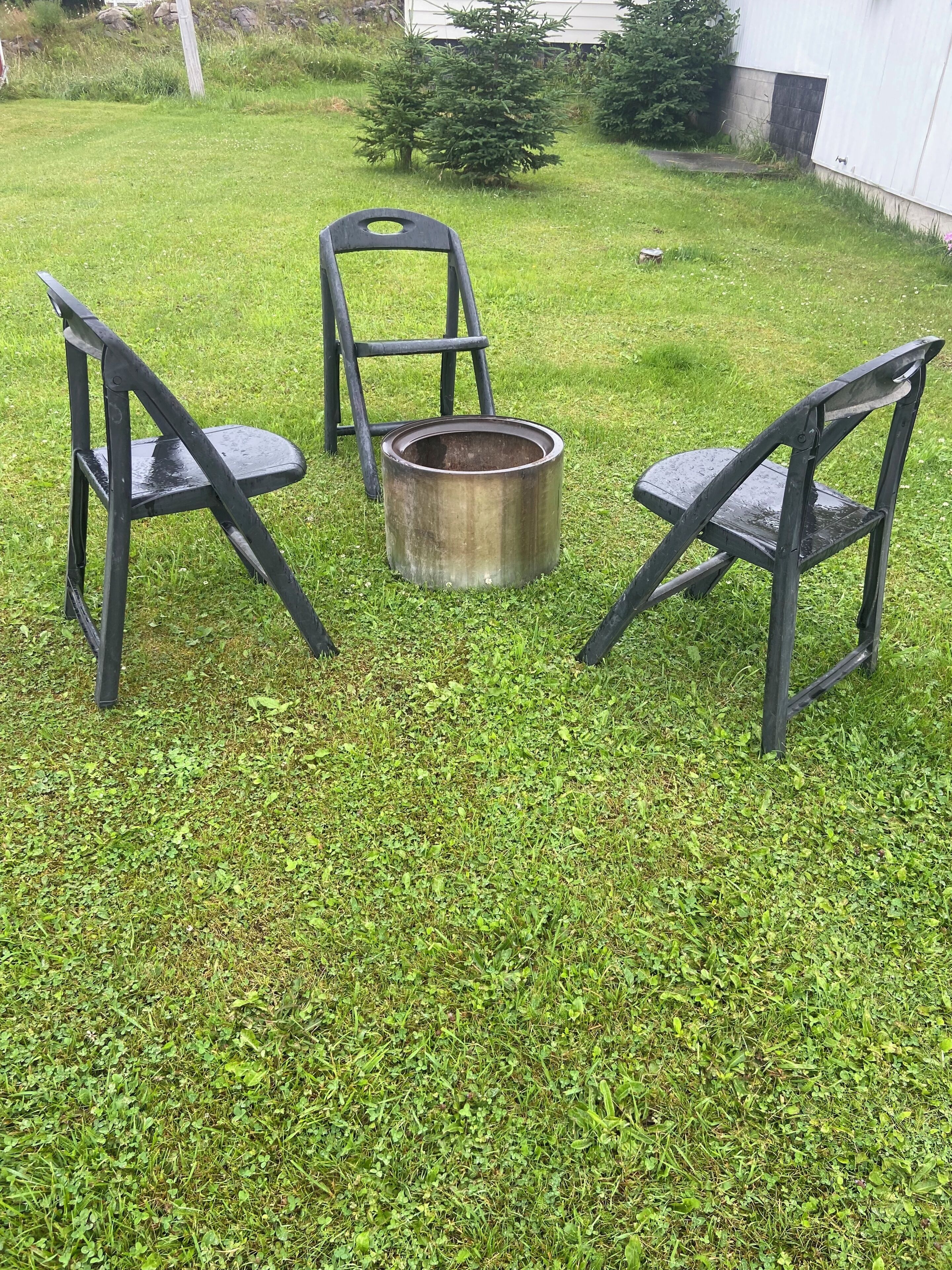 A grassy outdoor area with three metal chairs and a metal bucket.