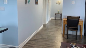A hallway with a wooden floor, a dining table with a chair, a wall clock, and a pendant light.