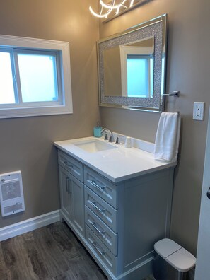A bathroom with a double sink vanity, a mirror with a decorative frame, a towel hanging on the wall, and a window. - Cozy home with lots of nature trails with ocean views close to all amenities.  (Port au Port East)