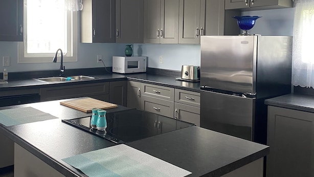 A modern kitchen with grey cabinets, a stainless steel refrigerator, a microwave, and a blue bowl on the counter.