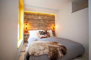 A bedroom with a wooden headboard, a bed with a gray blanket, a pillow with a floral design, and a cat on the bed. - Higgihaus 26 Clare Street Aparthotel (Bristol)