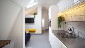 Una cocina moderna con horno empotrado, un lavamanos de acero inoxidable y una pequeña zona de comedor con un banco amarillo.