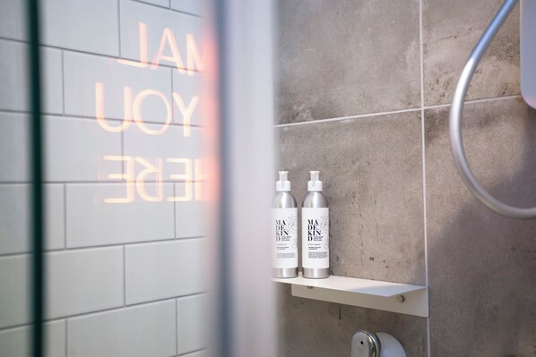 Et badeværelse med flisebeklædt væg, en hylde med to shampoo flasker og et brusehoved.