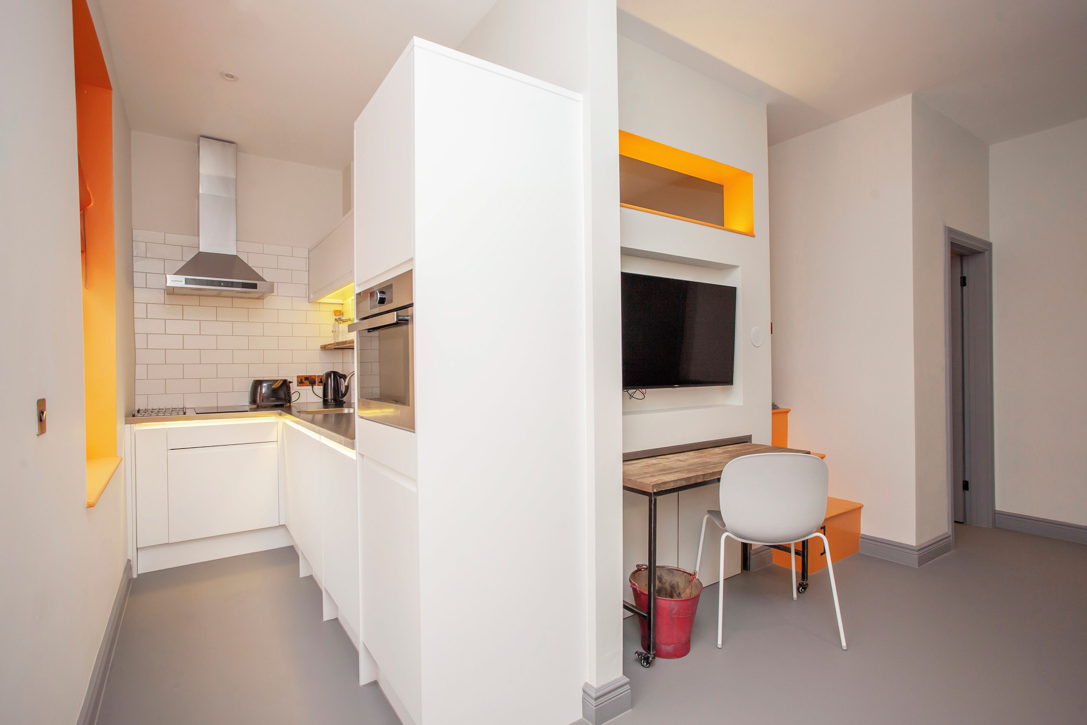 Een compacte keuken met witte kasten, een inbouwoven, een roestvrijstalen afzuigkap en een houten aanrechtblad.