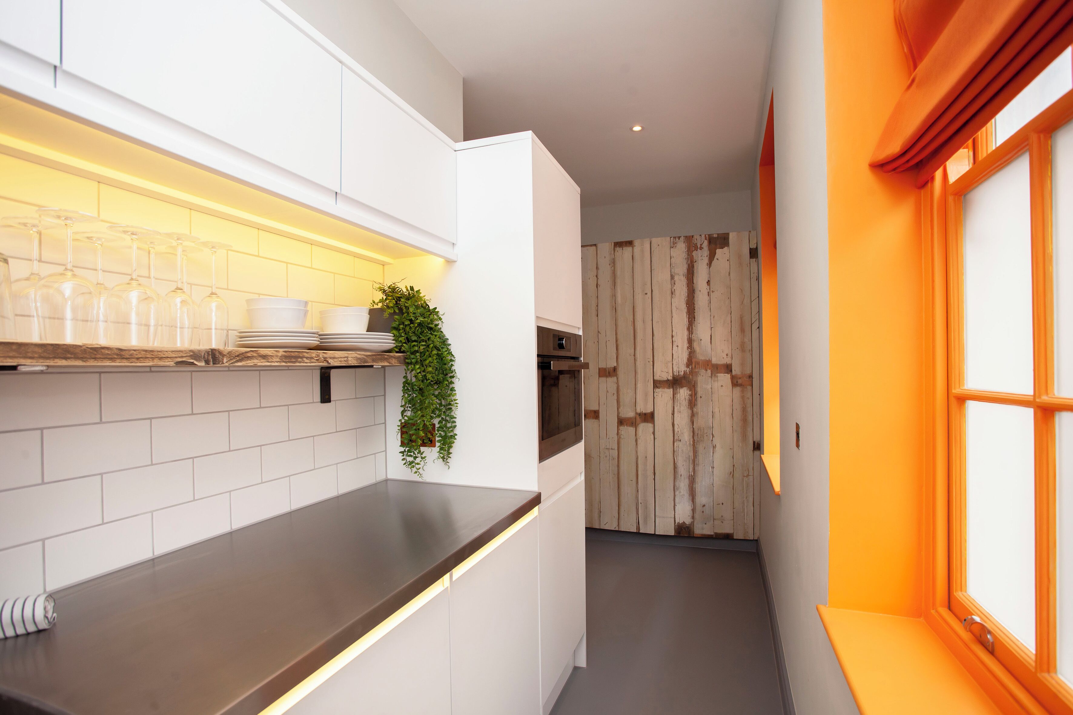 A modern kitchen with white cabinets, a dark countertop, and a wooden door in the background.