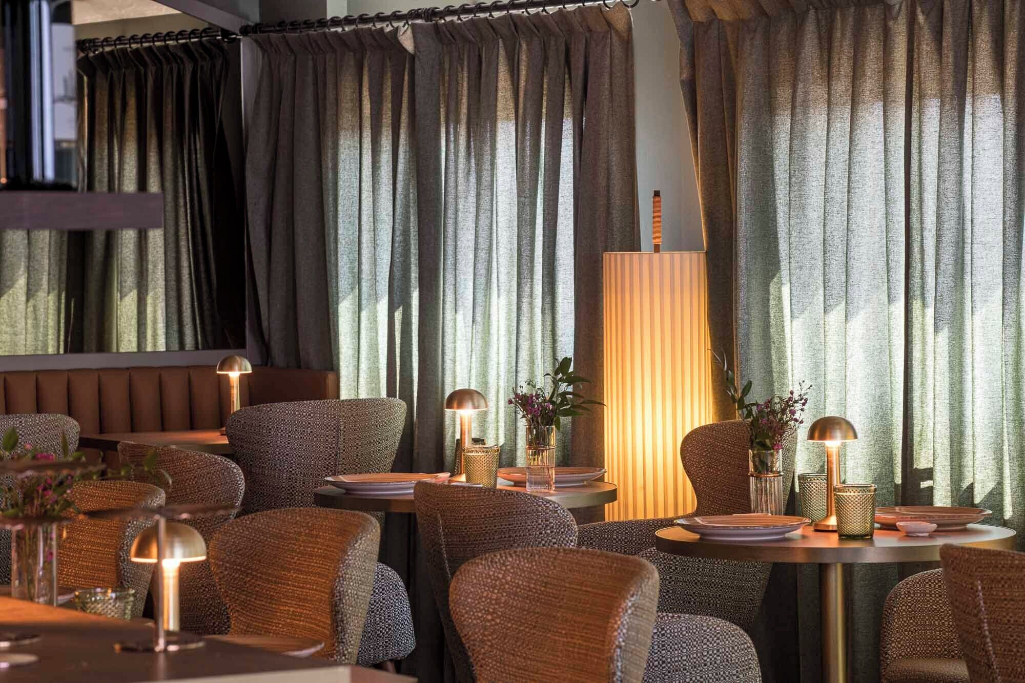 A restaurant with round tables, wicker chairs, and a large floor lamp.