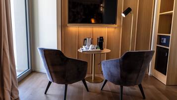 A modern room with two dark chairs, a small round table, a flat-screen TV mounted on the wall, and a floor lamp.