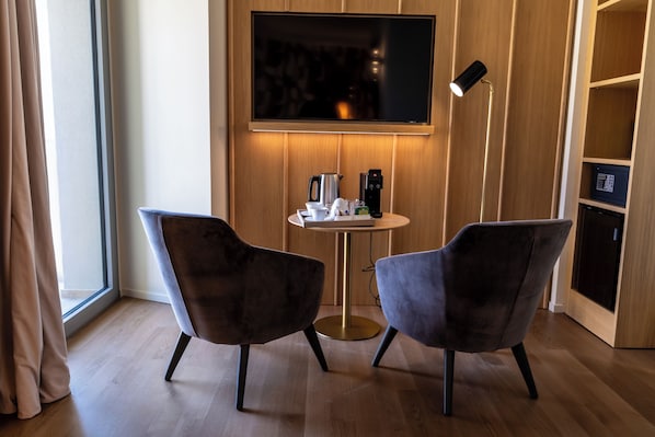 A modern room with two dark chairs, a small round table, a flat-screen TV mounted on the wall, and a floor lamp. - Columbus Urban Resort (Florence)