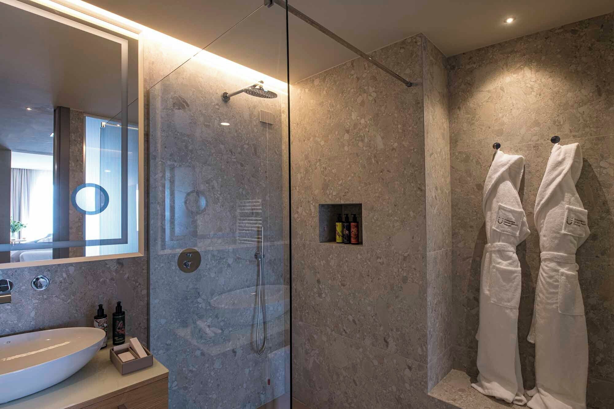 A modern bathroom with a glass-enclosed shower, a large mirror, and a vanity with toiletries.