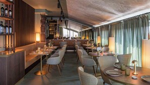 A restaurant with a bar area, seating with tables and chairs, and a view through large windows. - Columbus Urban Resort (Florence)