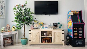 A living room with a wooden cabinet, a potted plant, a TV, and a colorful arcade machine.