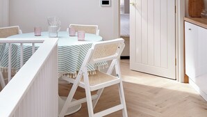 A cozy, well-lit room with a sloped ceiling, a dining table with chairs, a white door, and a small kitchen area. - Coach House Totnes: Natural Luxe (Totnes)