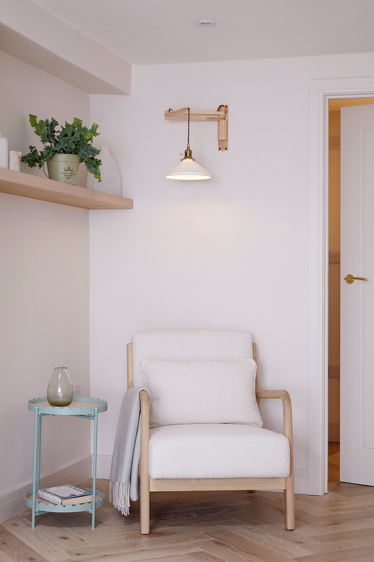 A room with a wooden chair, a small table with a pitcher, a hanging light fixture, and a door.