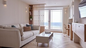 A modern living room with a sofa, coffee table, and a bookshelf. There is a sliding door leading to a balcony with a view. - Coach House Totnes: Natural Luxe (Totnes)