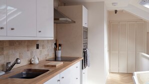 A modern kitchen with white cabinets, a wooden countertop, and a herringbone-patterned floor. - Coach House Totnes: Natural Luxe (Totnes)