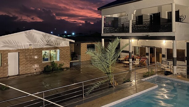 A modern two-story building with a swimming pool, a covered outdoor area, and a view of the sky at dusk.