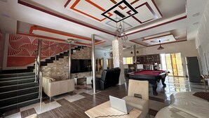A spacious living area with a pool table, a sofa, a laptop on a table, and a staircase with a geometric wall design.
