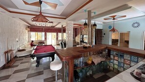 A spacious room with a pool table, a bar area with stools, and a seating area with a sofa and chairs.