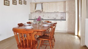 Un comedor con una mesa y sillas de madera, un jarrón con flores y armarios de color claro.