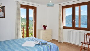 Un dormitorio con cama, cómoda, silla y vistas a montañas a través de amplios ventanales.