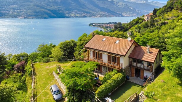 Una casa con techo de tejas rojas, un balcón y vistas a un lago y montañas.