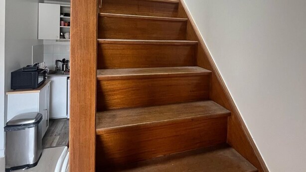 A wooden staircase leading to an upper floor, with a kitchen area visible on the landing.