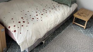 A bedroom with a sloped ceiling, a bed with a patterned bedspread, two pillows, and a small wooden nightstand.