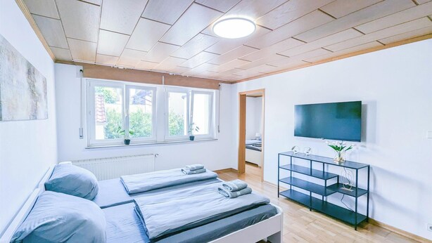 A modern bedroom with a bed, a TV, and a window with a view of greenery.