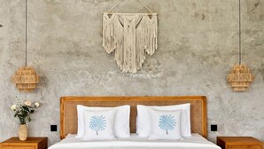 Un dormitorio con pared de concreto, un colgador de macramé, dos lámparas de noche, un cabecero de madera y una mesita de noche con un jarrón de flores.