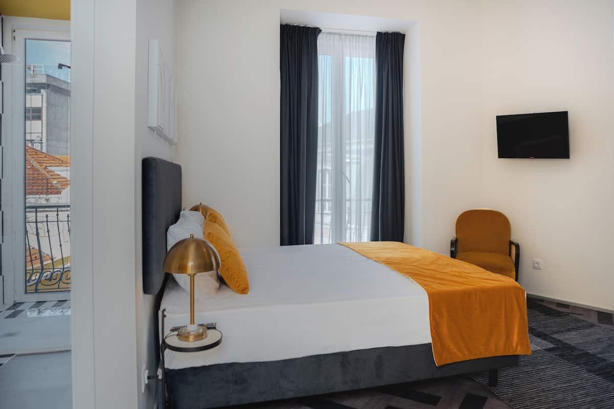 A hotel room with a bed, a desk, a chair, a TV, and a window with curtains.