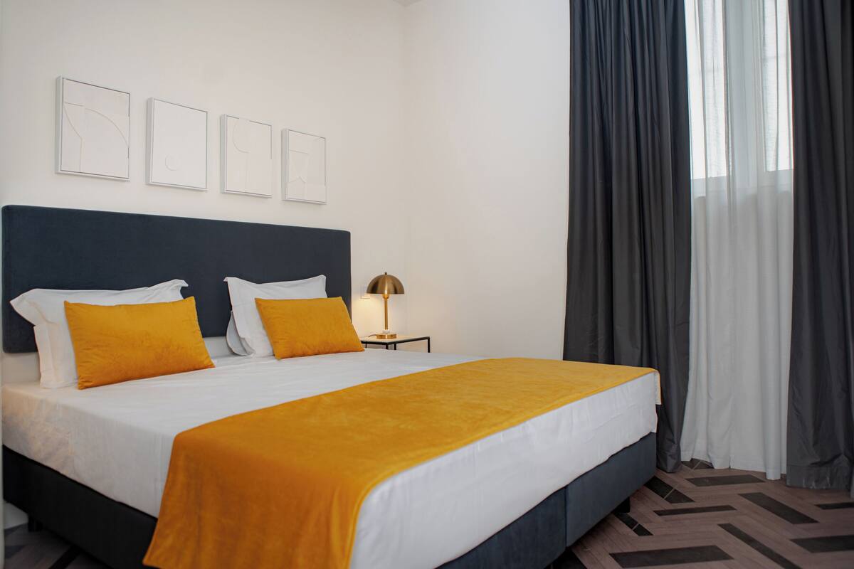 A hotel room with a bed, a nightstand, a lamp, and a window with curtains.