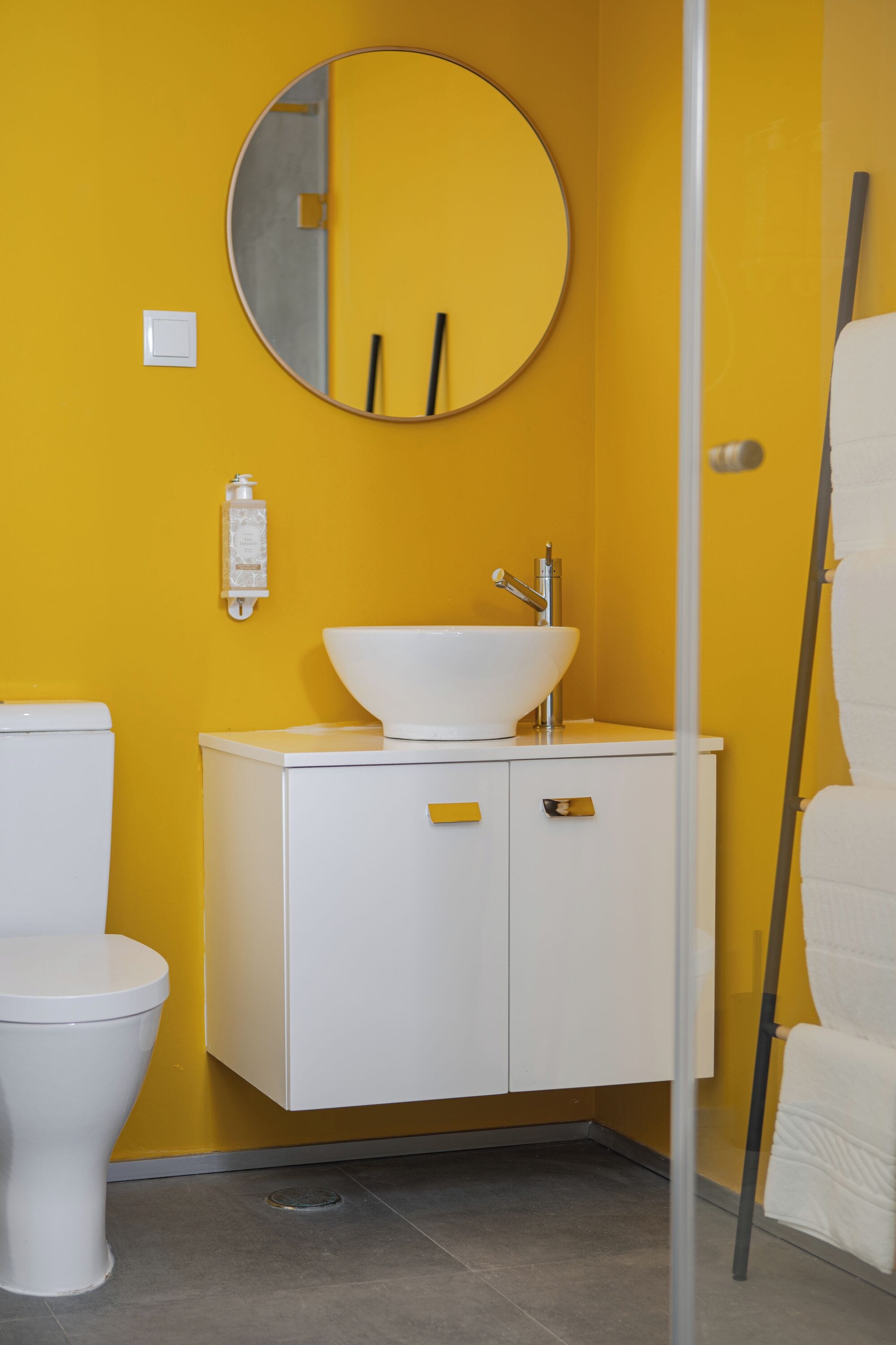 A bathroom with a yellow wall, a white sink, and a round mirror.