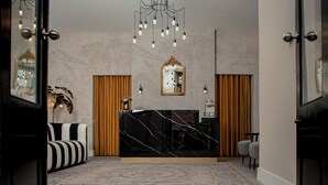 Zona de recepción de un hotel con un mostrador de mármol, un espejo grande y una araña.