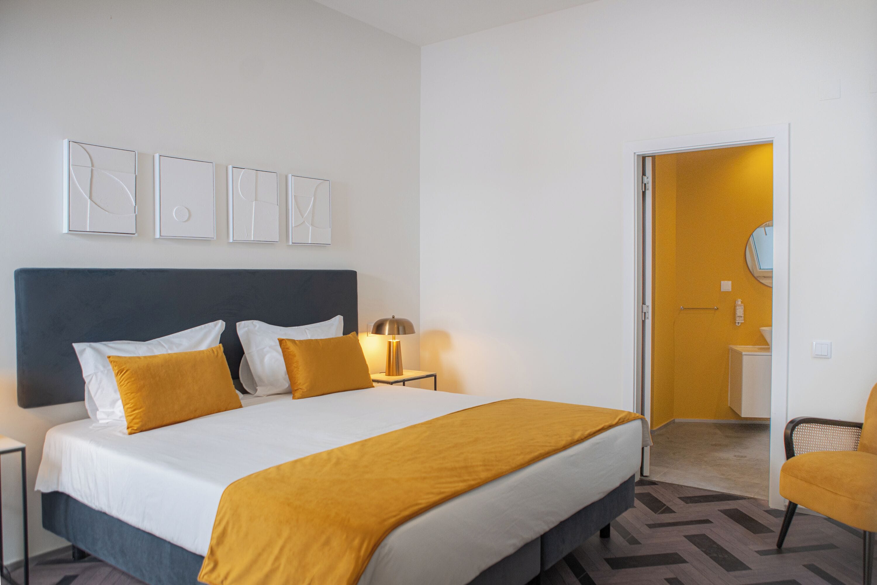 Ein Hotelzimmer mit einem großen Bett, einem Nachttisch, einem Sessel und einem durch eine offene Tür einsehbarer Badezimmer.