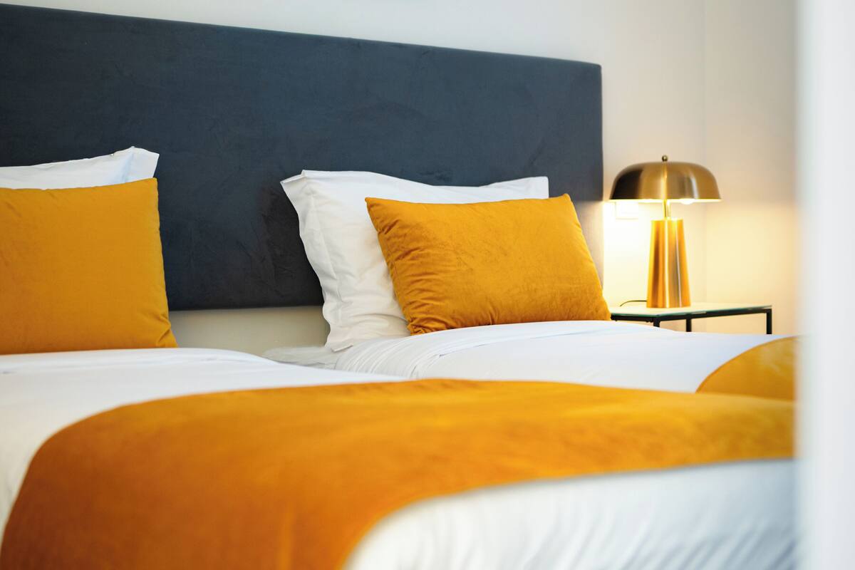 A hotel room with a large bed, two pillows, a bedside table, and a lamp.