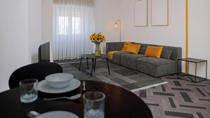 Una sala de estar moderna con un sofá gris, una mesa de centro y un comedor con una mesa preparada para dos.